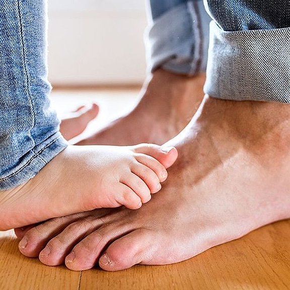 Die Füße eines Kleinkindes stehen auf den Füßen einer erwachsenen Person.