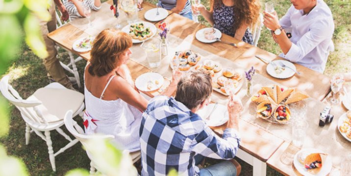 Eine große Familie sitzt im sommerlichen Garten an einem gedeckten Tisch und isst.