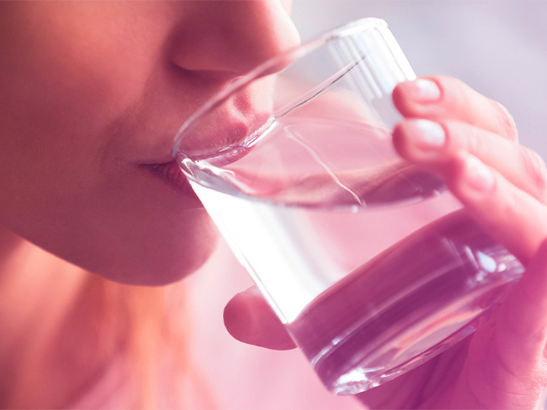 Eine Person führt ein gefülltes Wasserglas an ihre Lippen.
