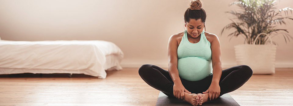Eine Schwangere sitzt im Schneidersitz auf einer Yogamatte.