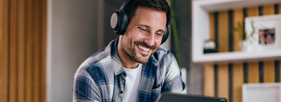 Ein Mann mit Kopfhörern hält lächelnd ein Tablet in der Hand.