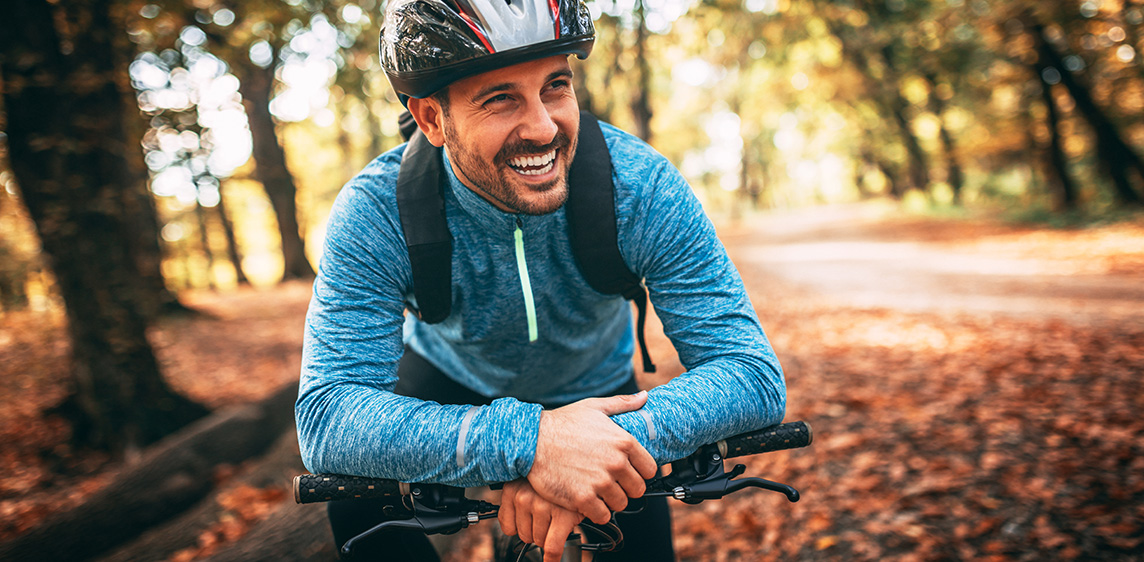 Ein Mann in Sportbekleidung macht eine Radtour durch einen herbstlichen Wald.