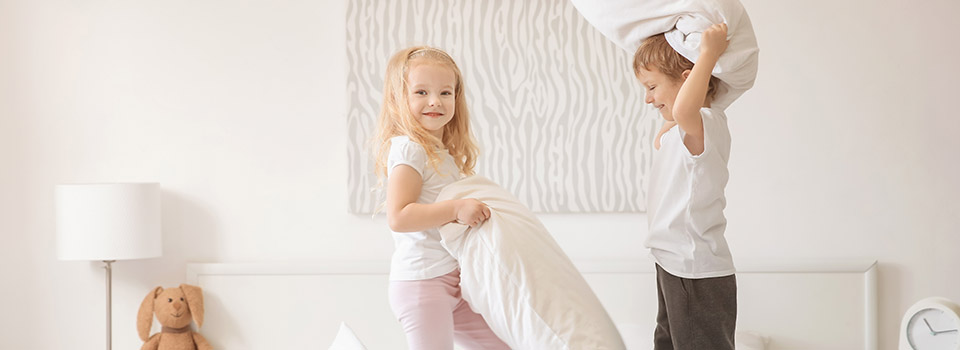 Ein Junge und ein Mädchen stehen auf einem Bett und haben jeweils ein Kissen in der Hand.