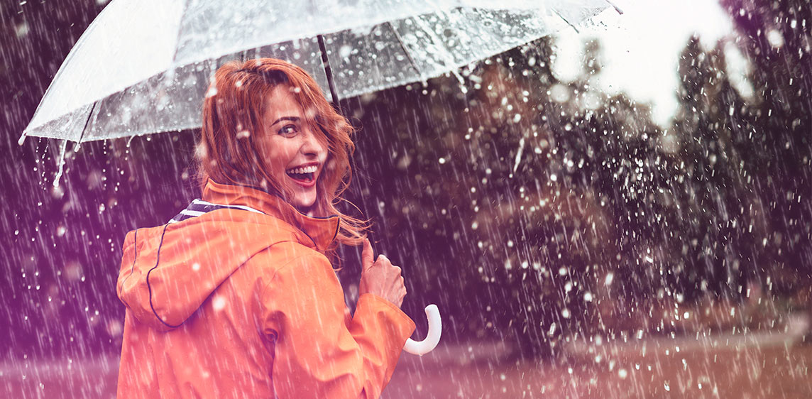 Eine Frau dreht sich um und lächelt. Sie steht im Regen mit einem Regenschirm.