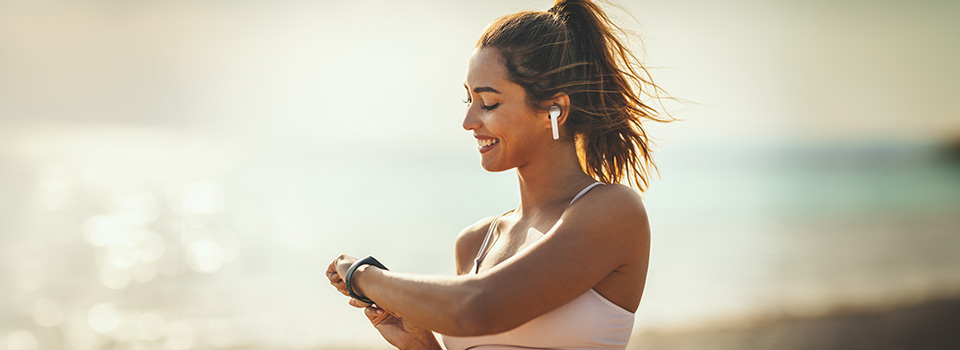 Eine Frau mit Kopfhörern schaut lächelnd auf ihre Fitnessuhr.