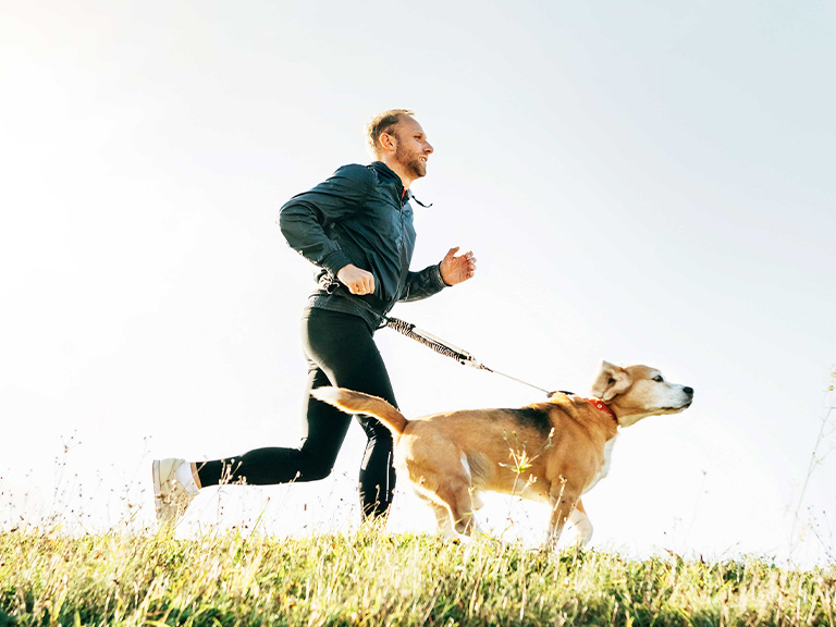 Ein Mann mittleren Alters joggt mit seinem Hund an der Leine im Freien.