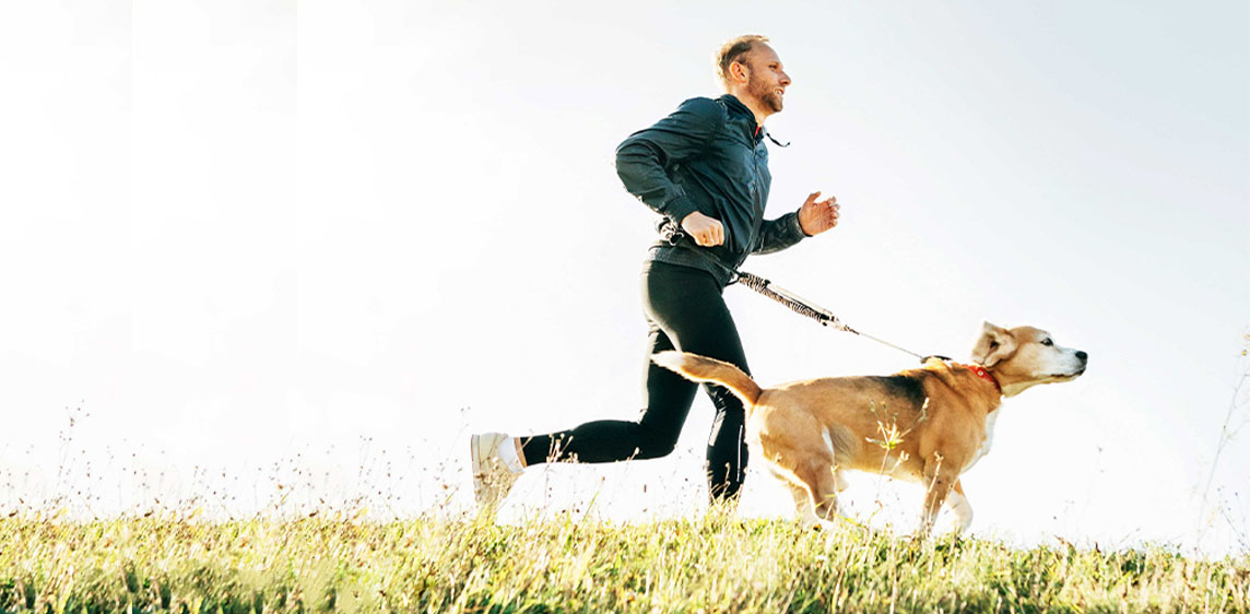 Ein Mann joggt mit einem Hund über eine Wiese