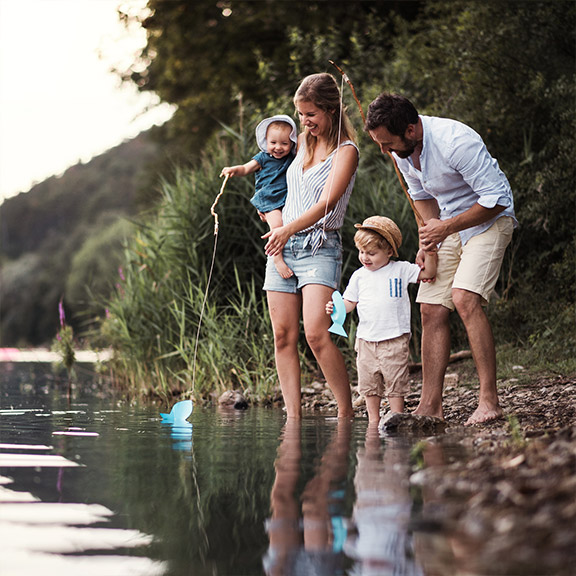 Ein junges Paar steht mit seinen zwei Kindern an einem See.