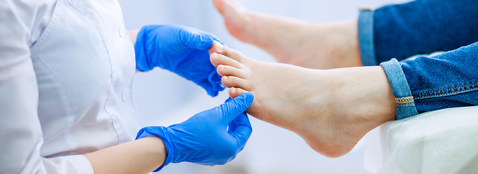 Eine Person im Kittel und mit Latexhandschuhen untersucht einen Fuß.