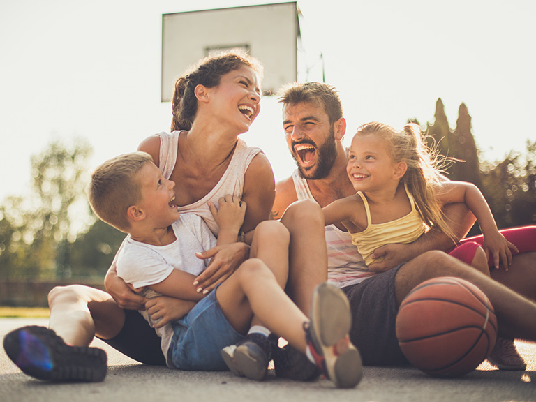 Eine Familie sitzt auf einem Basketball-Feld und lacht.