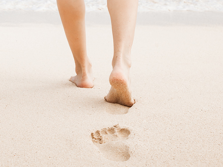 Eine Person spaziert am Strand entlang und hinterlässt Fußspuren im Sand.