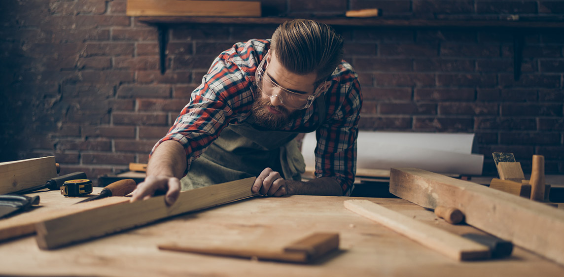 Ein Handwerker bearbeitet ein Stück Holz in seiner Werkstatt.