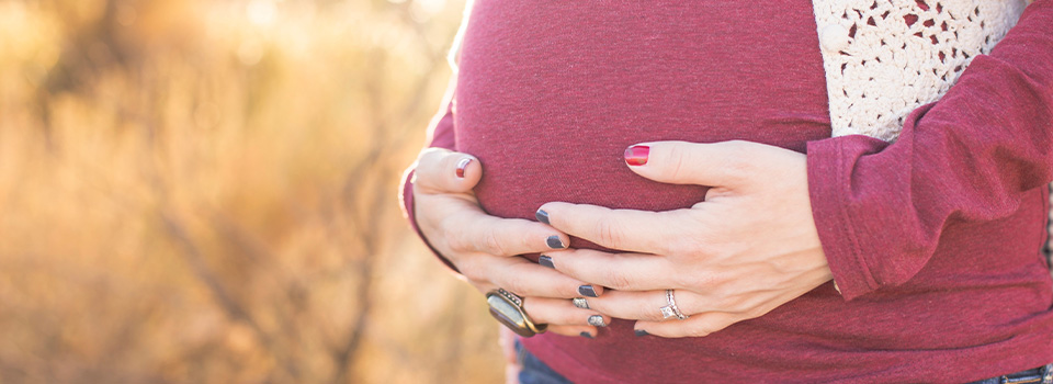 Eine Schwangere hat beide Hände schützend auf ihren Bauch gelegt.